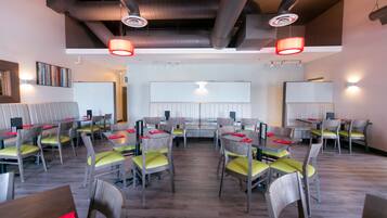 Ein Restaurant mit mehreren Tischen und Stühlen, einer hohen Decke mit freiliegenden Lüftungsrohren und einer neutralen Farbgestaltung.