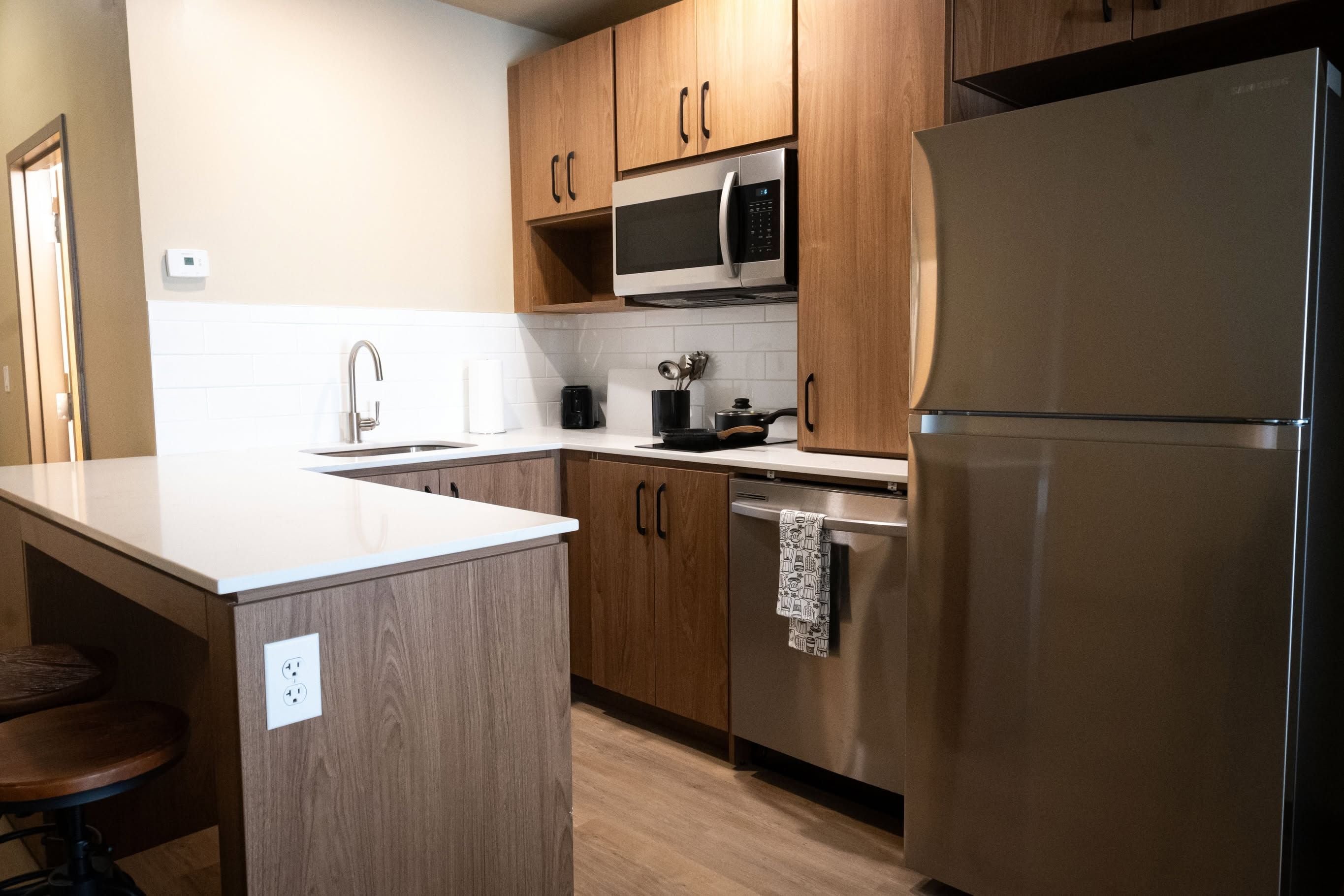 A modern kitchen with wooden cabinets, a stainless steel refrigerator, a microwave, and a sink.
