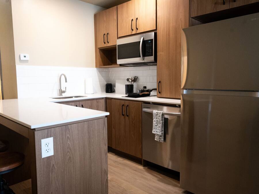 A modern kitchen with wooden cabinets, a stainless steel refrigerator, a microwave, and a sink.