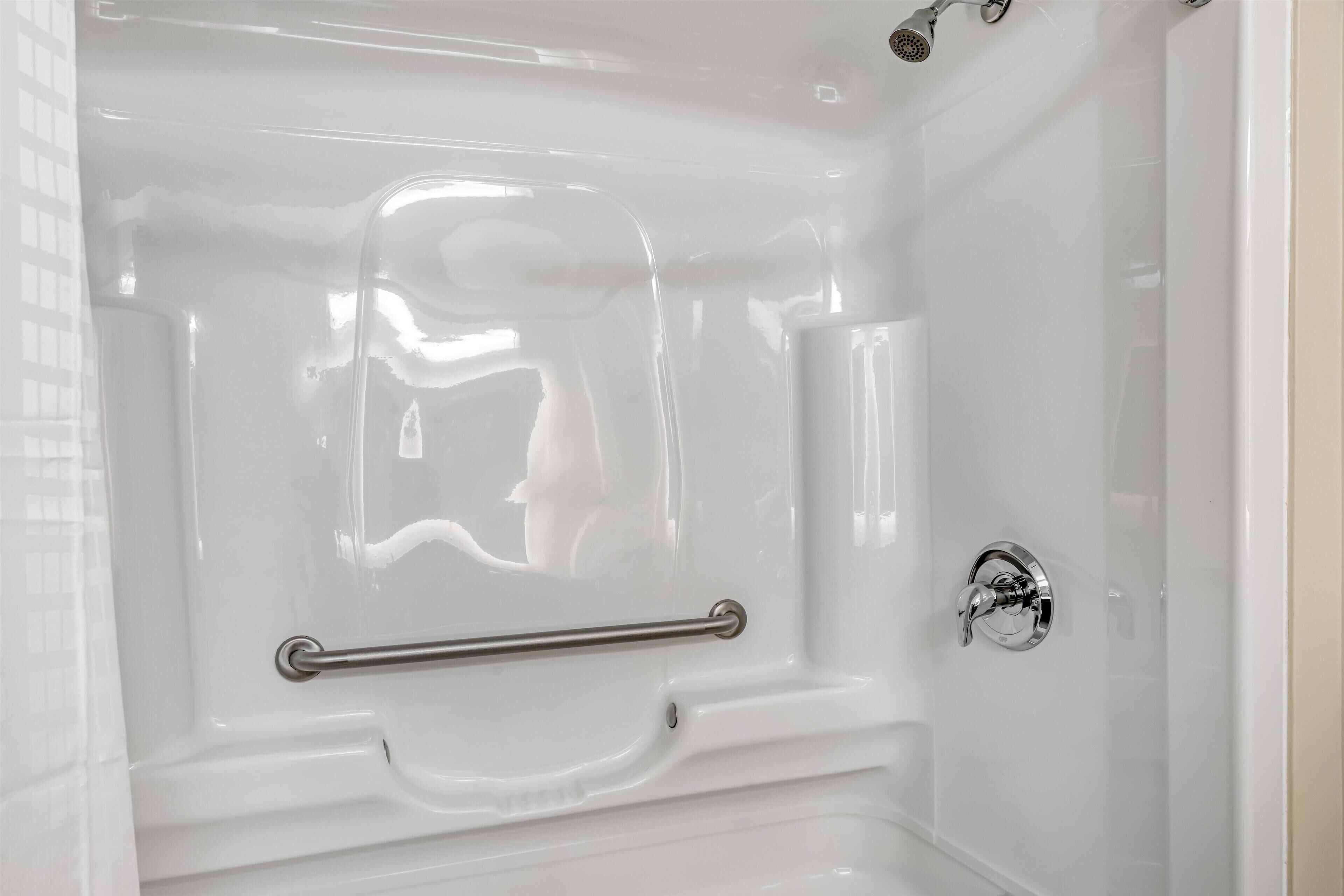 Una bañera blanca con una barra de apoyo, un cabezal de ducha y un grifo.