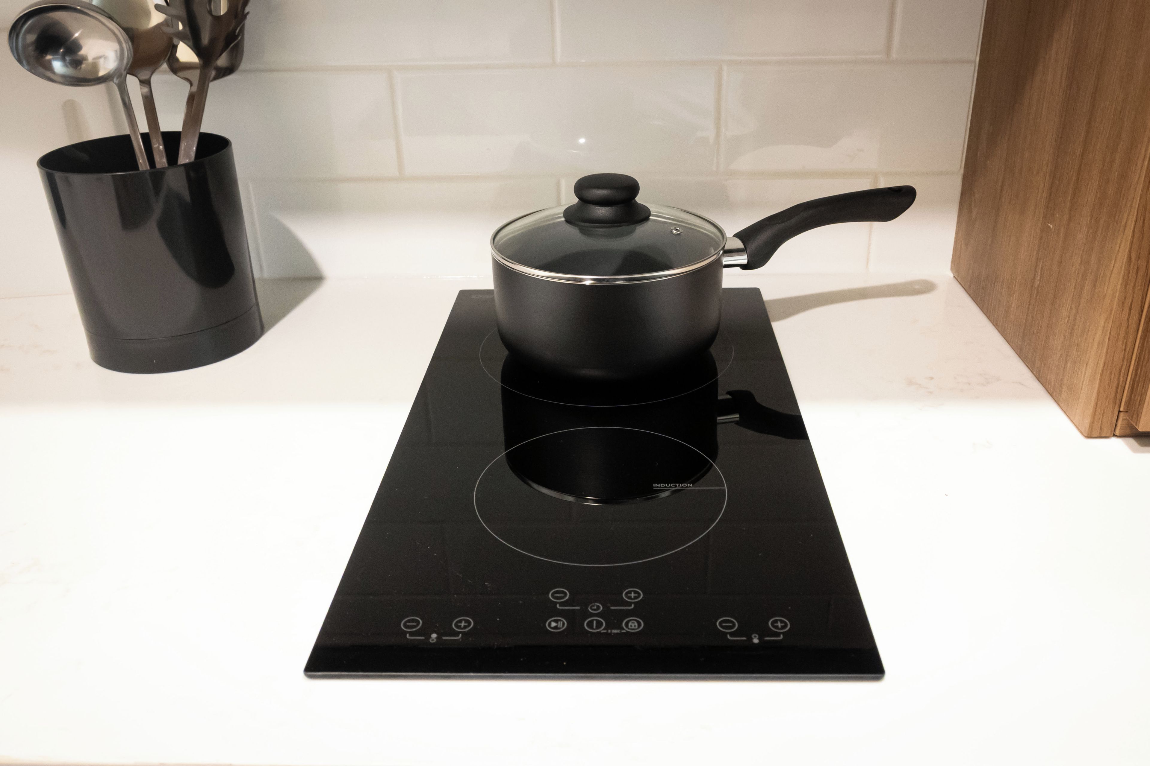 A black induction cooktop with a pot on it, a black pot holder, and a utensil holder with spoons.