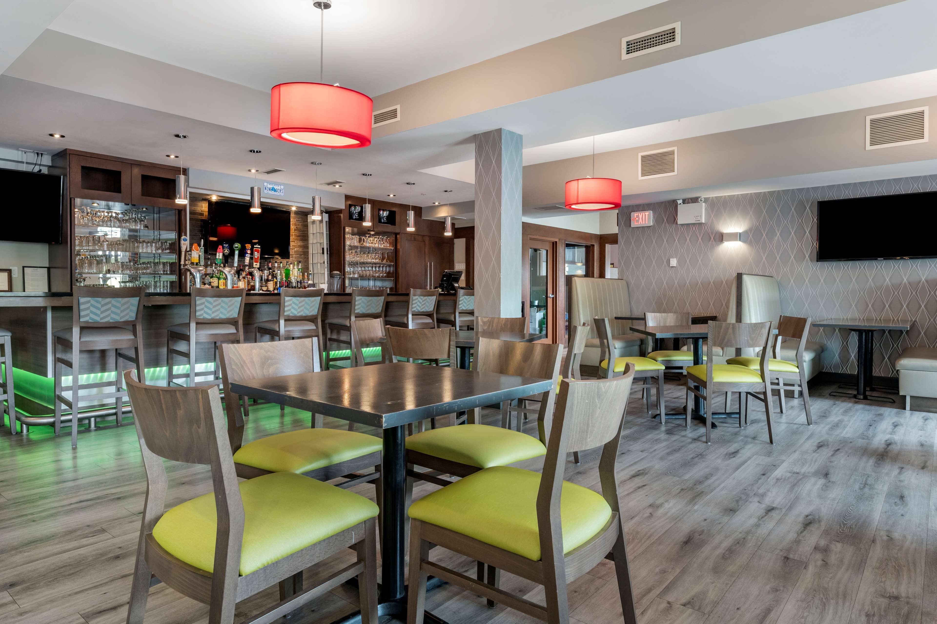 A restaurant with wooden tables and chairs, a bar area with shelves of bottles, and a television mounted on the wall.