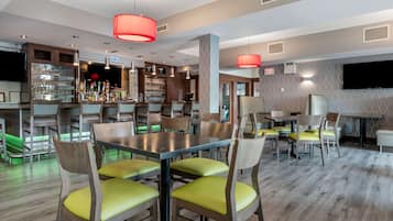 A restaurant with wooden tables and chairs, a bar area with shelves of bottles, and a television mounted on the wall.