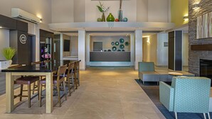 A spacious living area with a high ceiling, a dining table with chairs, a fireplace, and a seating area with a patterned ottoman. - Best Western Plus Dartmouth Hotel & Suites (Dartmouth)