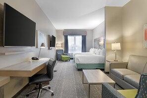 Een hotelkamer met een bureau, twee bedden, een bank, een televisie en een raam met gordijnen.