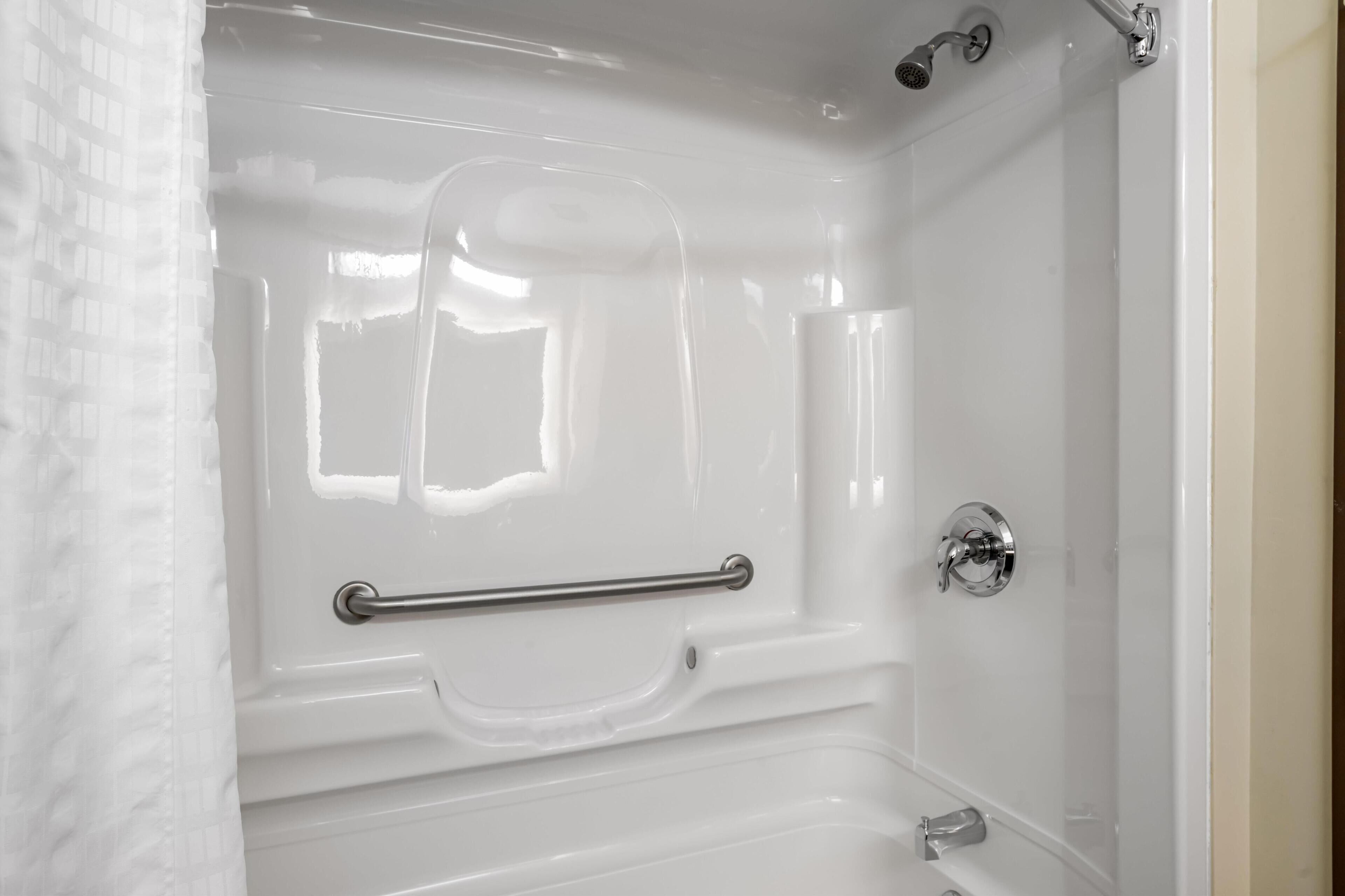 A white bathtub with a grab bar, a showerhead, and a faucet.