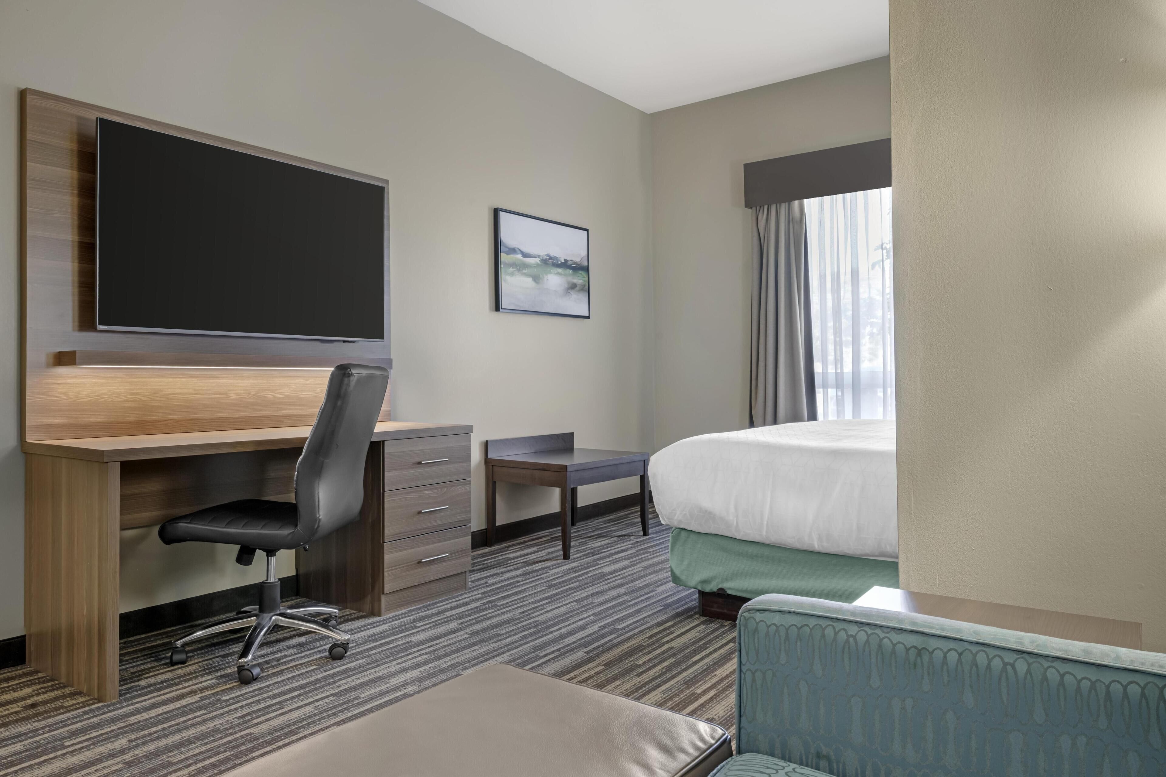 A hotel room with a large bed, a desk with a chair, a television, and a framed picture on the wall.