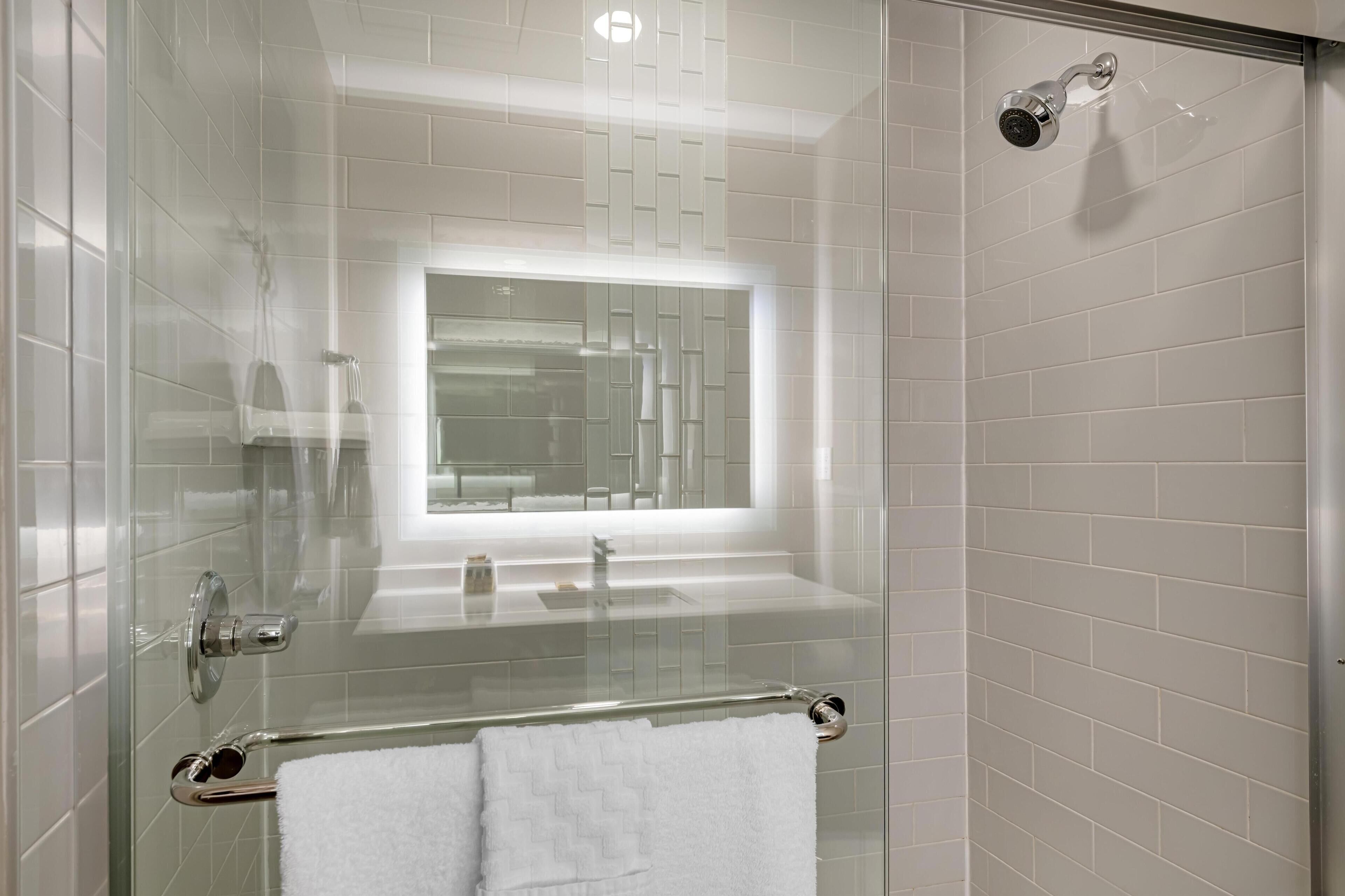 Ein modernes Badezimmer mit einer gläsernen Dusche, einem Waschtisch ebenfalls mit Glasabdeckung und einer Glastür.