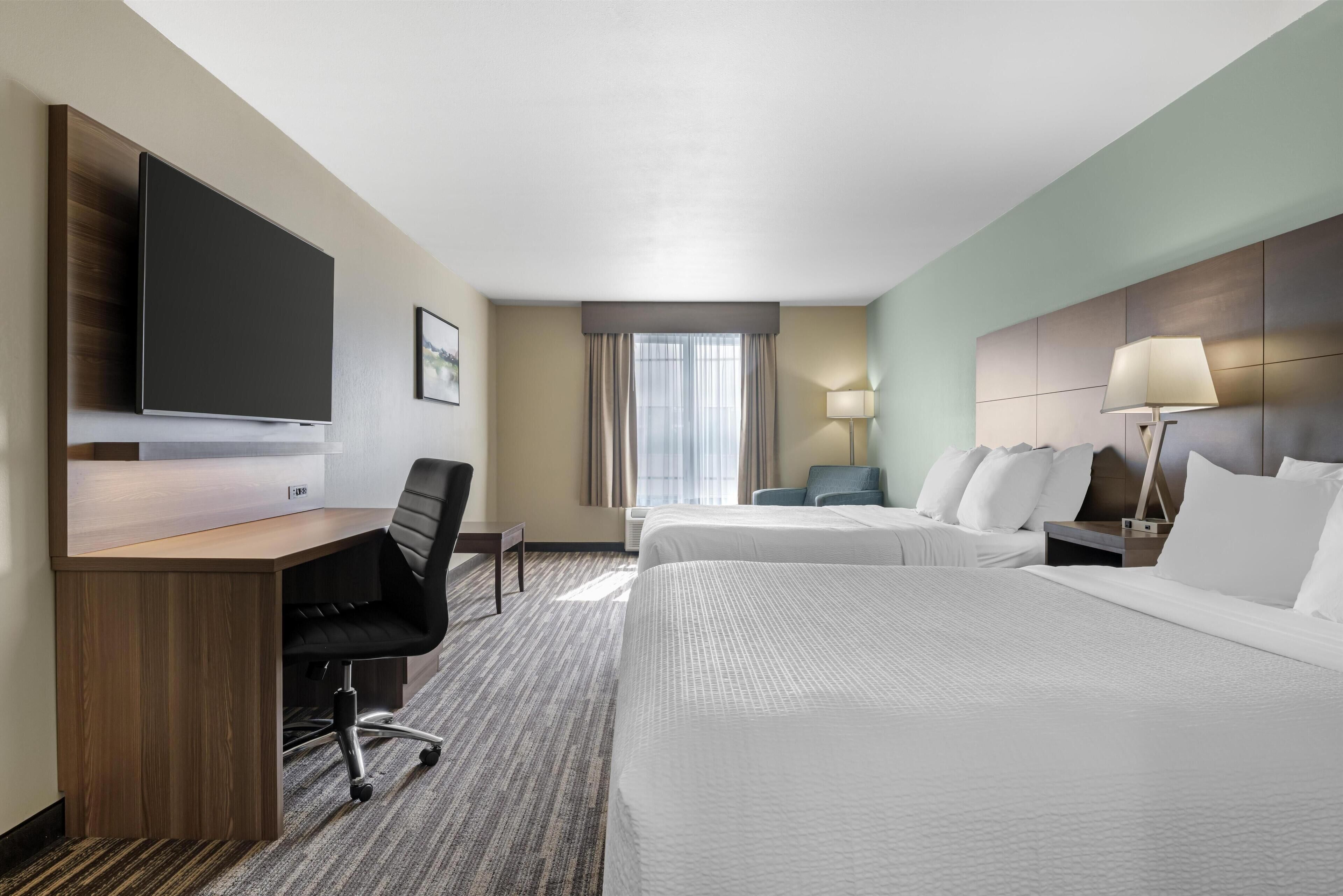 Una habitación de hotel con escritorio, dos camas, televisor y lámpara.