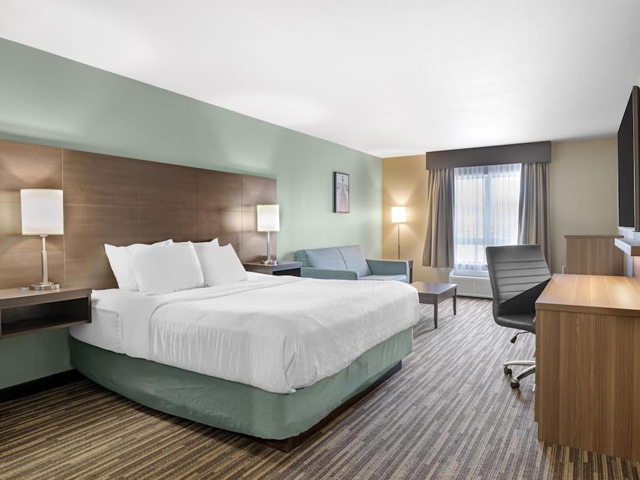 A hotel room with a large bed, a desk, a chair, a TV, and a window with curtains.