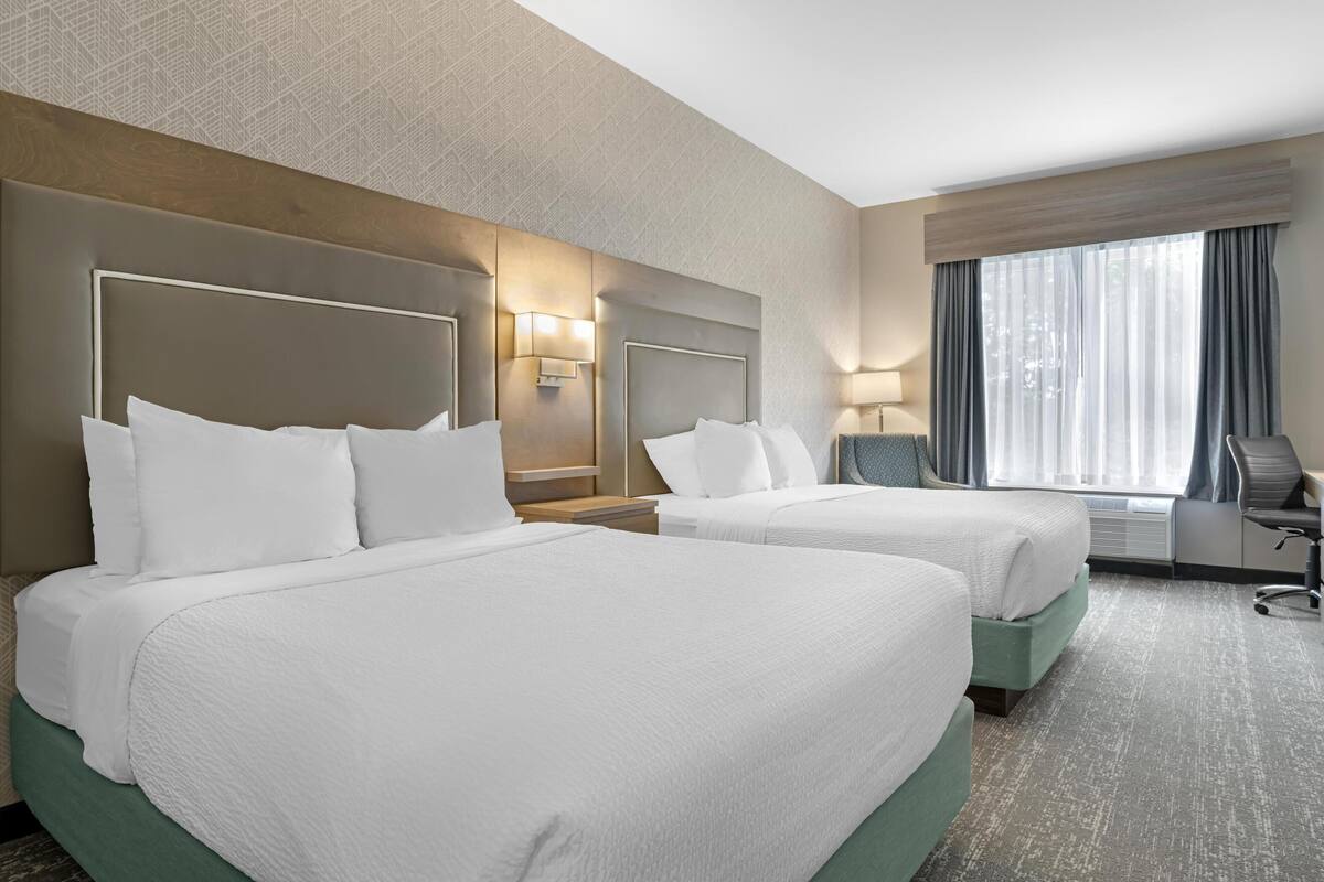 Een hotelkamer met twee bedden, een bureau, een stoel en een groot raam met gordijnen.