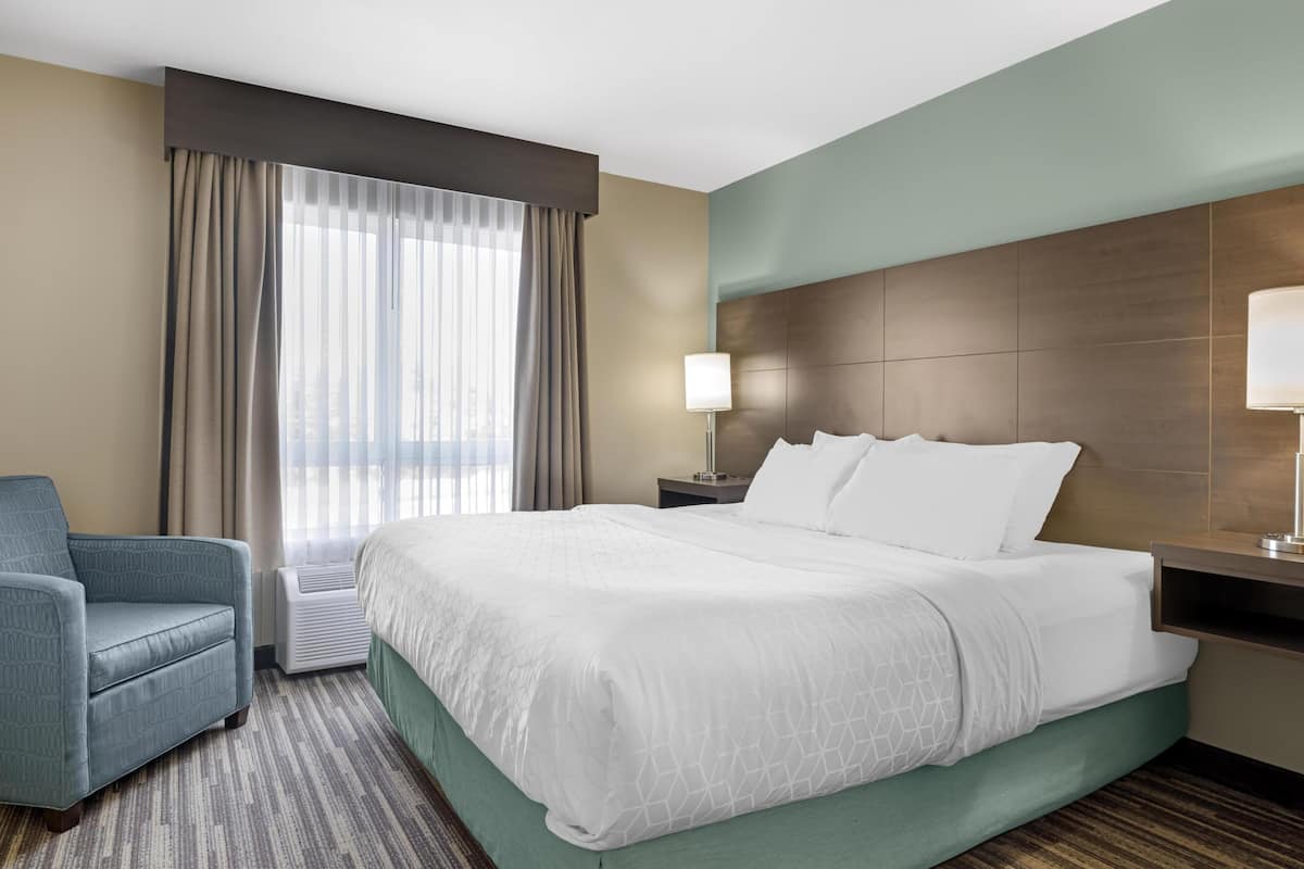 Een hotelkamer met een groot bed, een stoel, een nachtkastje, een lamp en een raam met gordijnen.