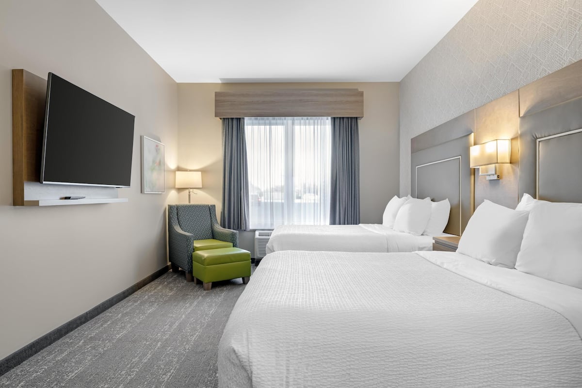 Hotelkamer met twee bedden, een flatscreen televisie, een bureau, een stoel en een raam met gordijnen.