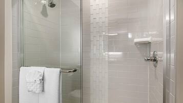 A modern bathroom with a glass shower enclosure, white tiled walls, and a visible towel rack with a folded towel.