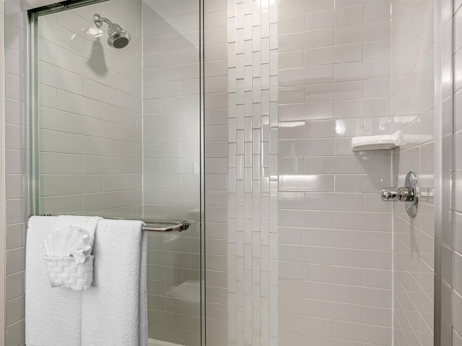 A modern bathroom with a glass shower enclosure, white tiled walls, and a visible towel rack with a folded towel.