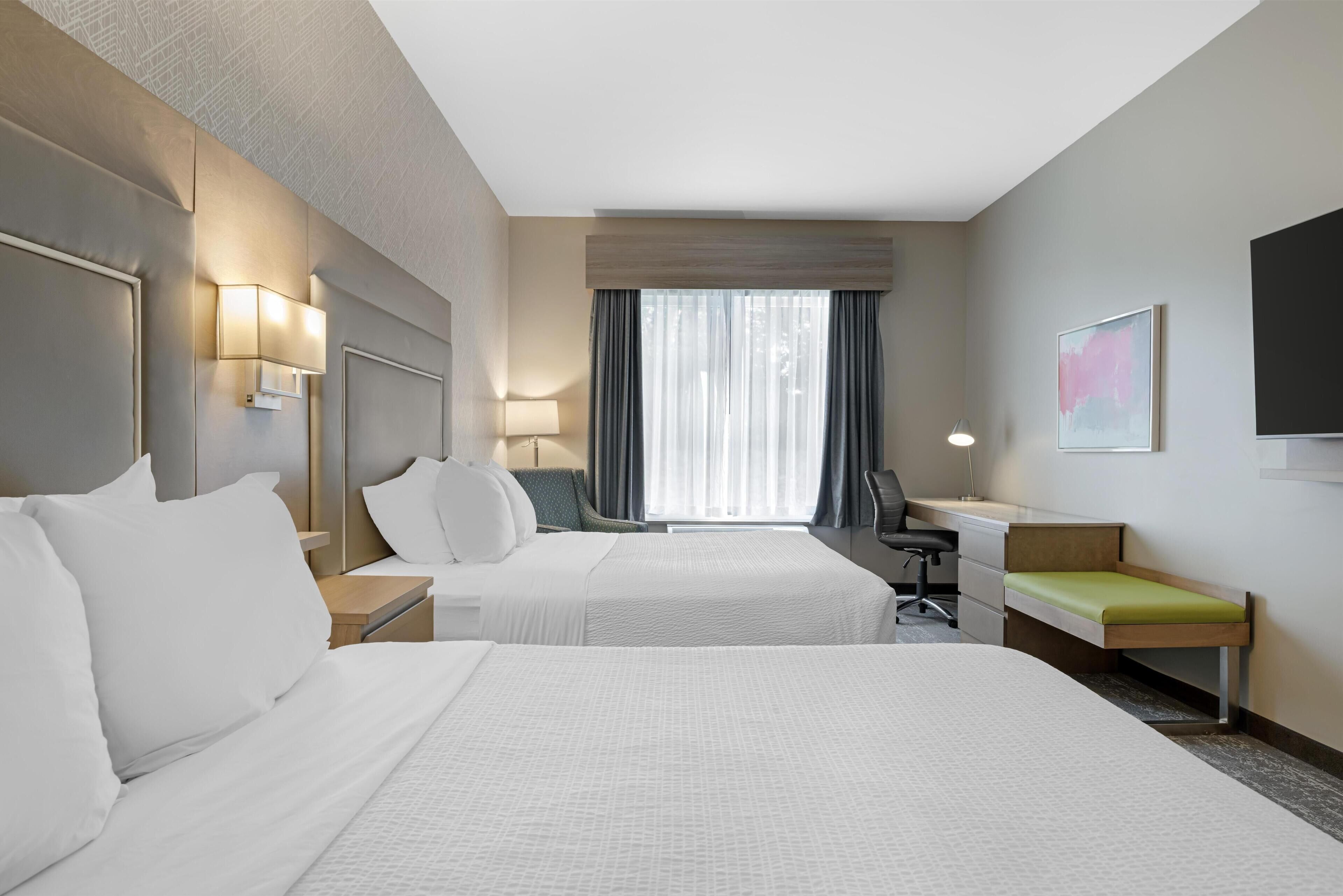 Habitación de hotel con dos camas, un escritorio, una silla, un televisor y una ventana con cortinas.