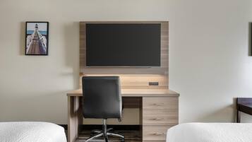 A hotel room with a wooden desk, a black office chair, two beds, and a framed picture on the wall.