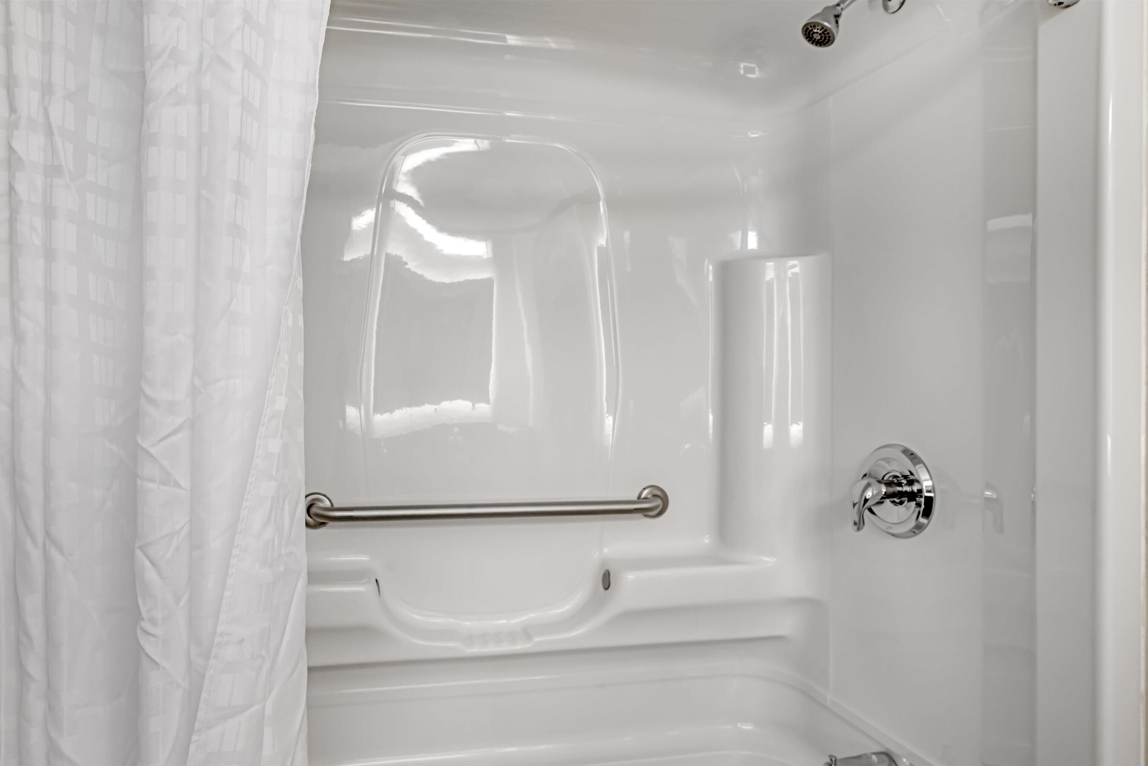 A white bathtub with a grab bar, a showerhead, and a chrome faucet.