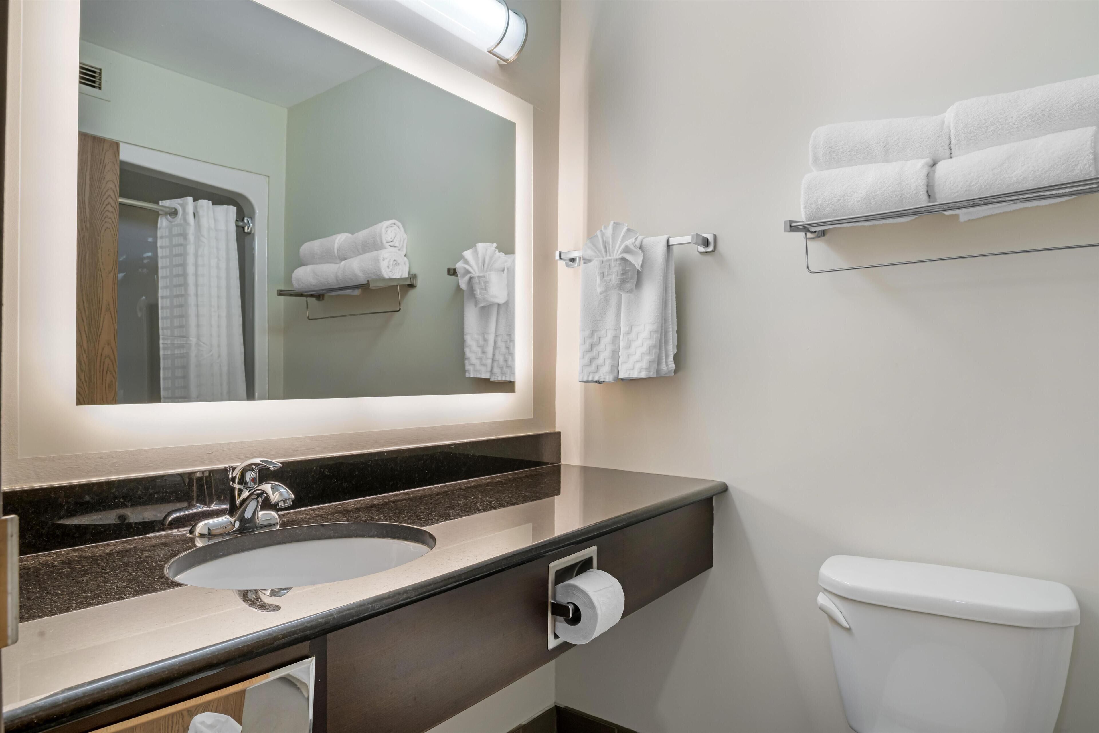 Un baño con lavamanos, espejo, toallero y retrete.