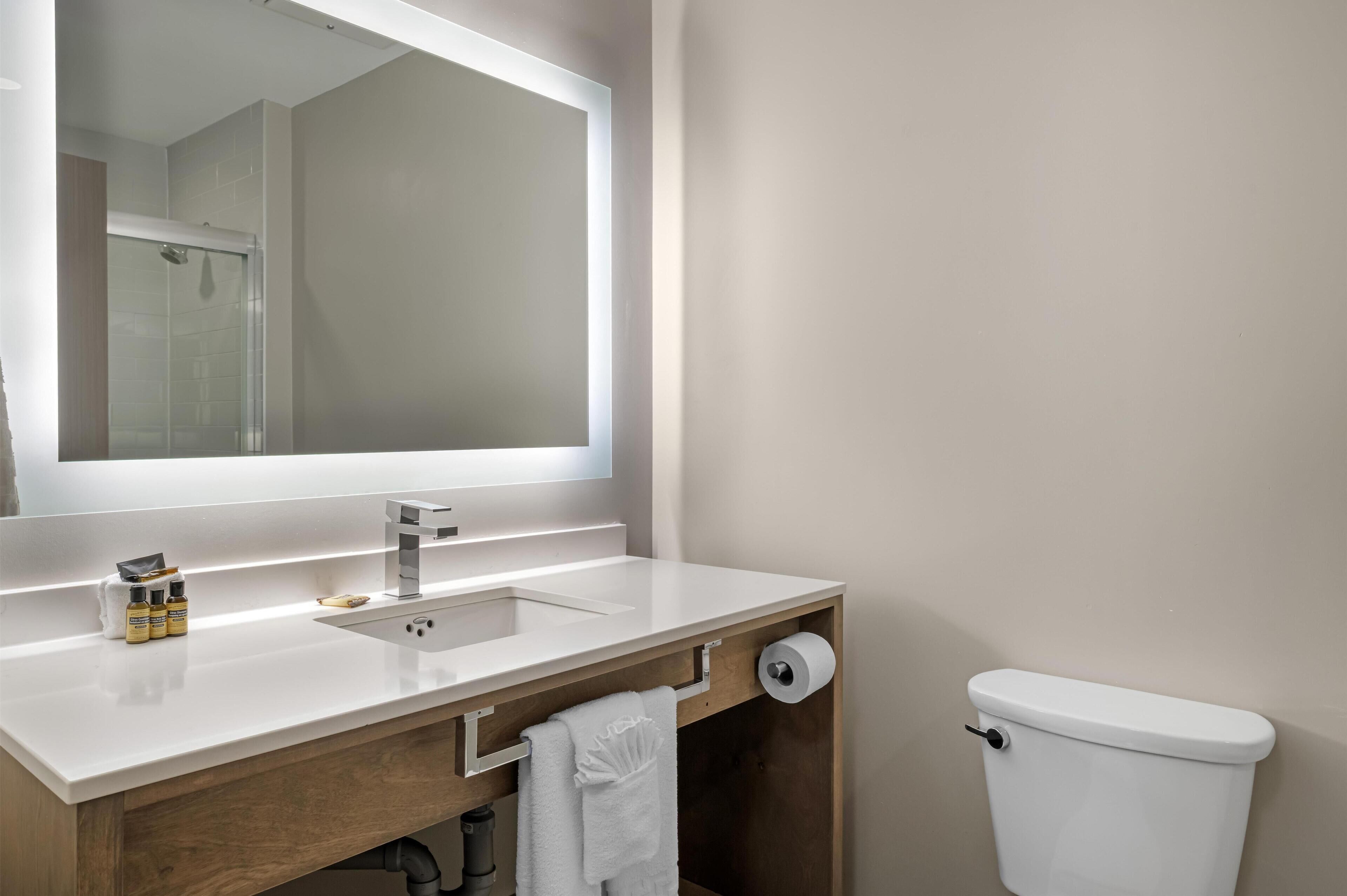 A modern bathroom with a white sink, mirror, and toilet.