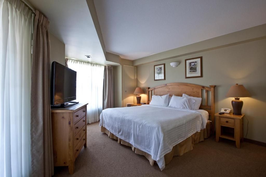 A hotel room with a large bed, a television on a wooden dresser, two bedside lamps, and a framed picture on the wall.