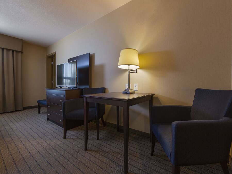 Una habitación de hotel con escritorio, dos sillas, lámpara, cómoda y televisor.
