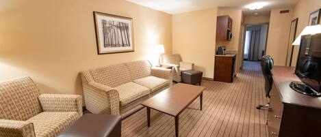 A hotel room with a patterned sofa set, a small table, a desk with a chair, and a framed picture on the wall.