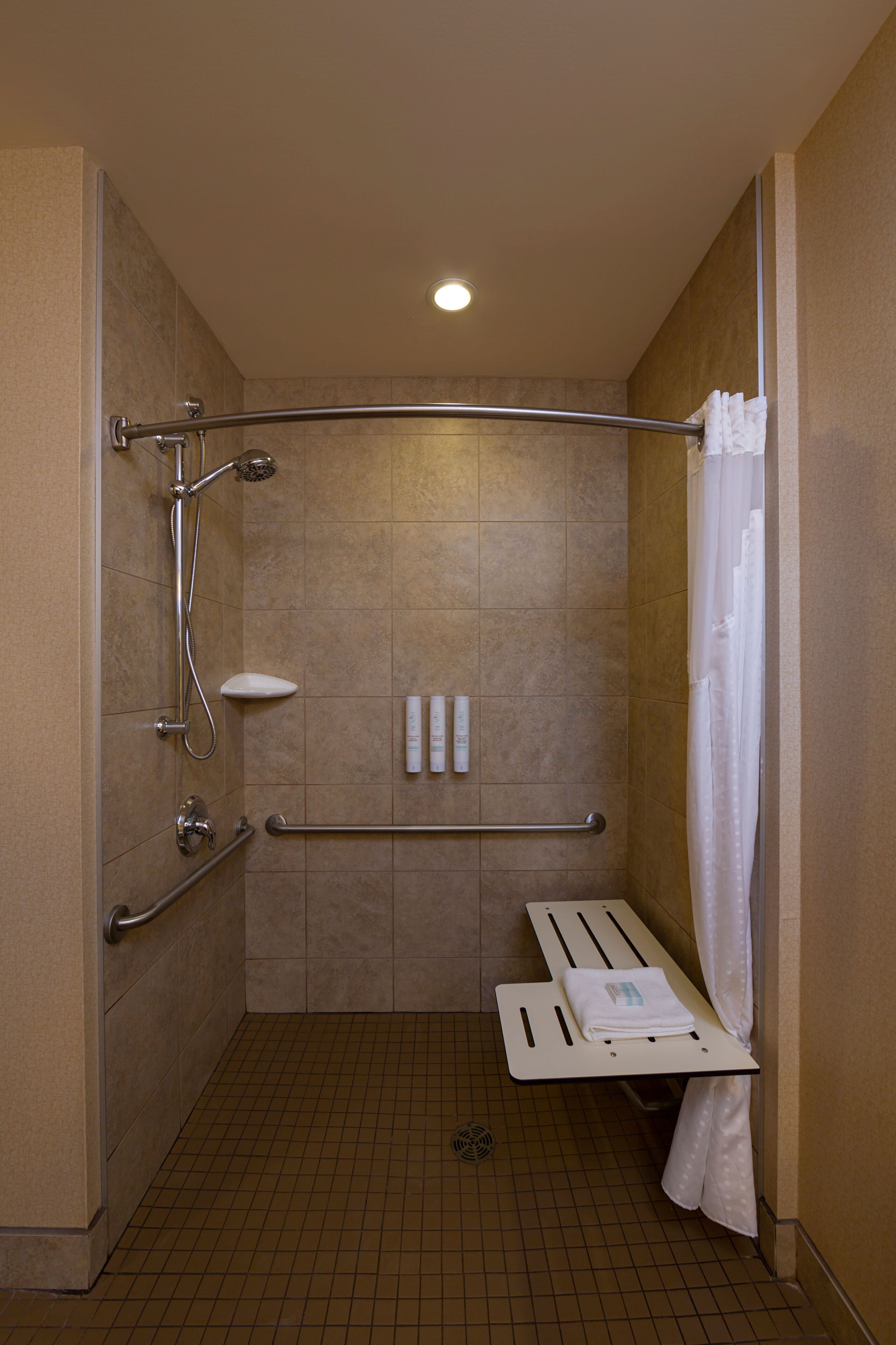 A shower area with a grab bar, a bench, and a showerhead.