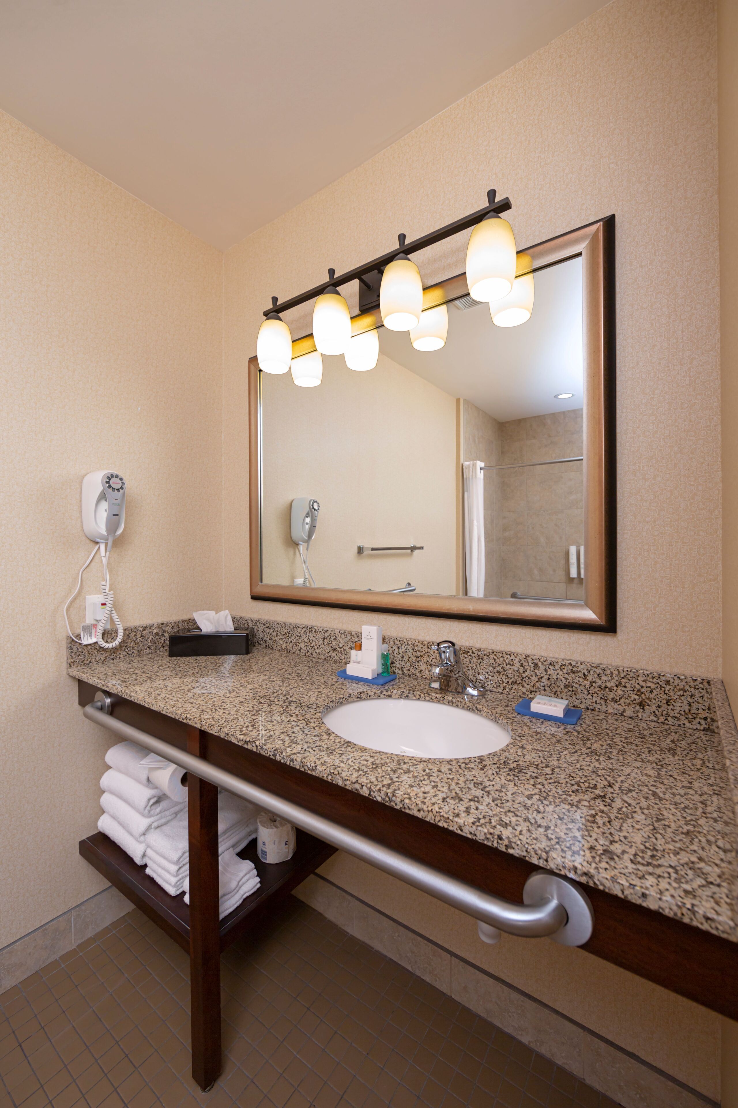 Un baño con encimera de granito, un lavabo blanco, toallero, espejo con iluminación y secador de pelo.