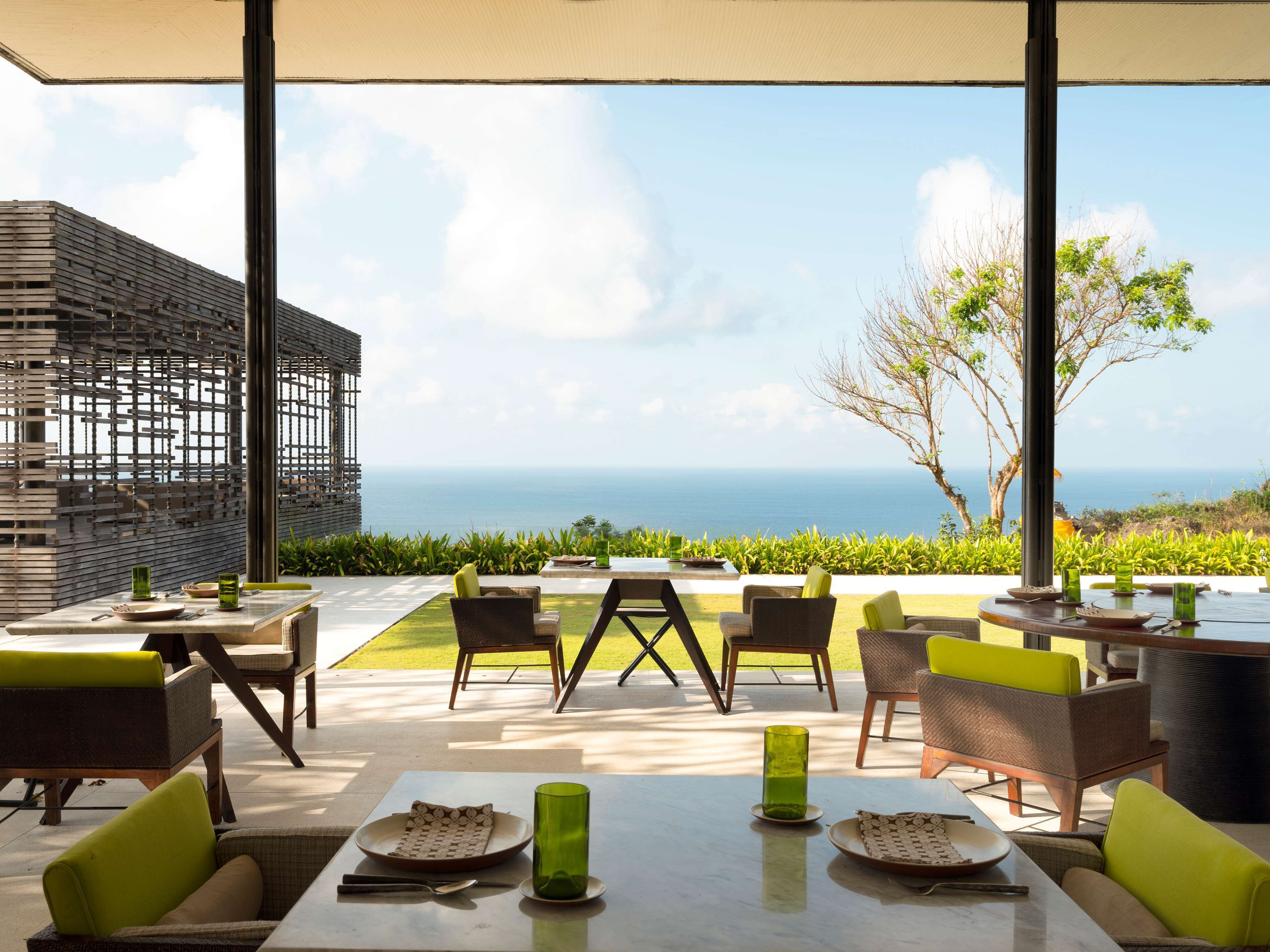 An outdoor dining area with tables and chairs, a view of the ocean, and a modern architectural design.