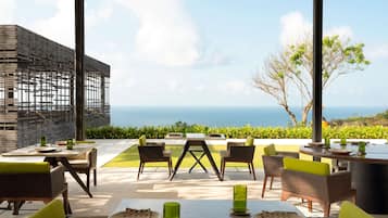 Un área de comedor al aire libre con mesas y sillas, vista al océano y un diseño arquitectónico moderno.