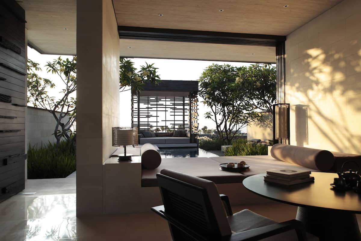 A modern interior with a dining area, a sofa, and a view of a garden and building outside.