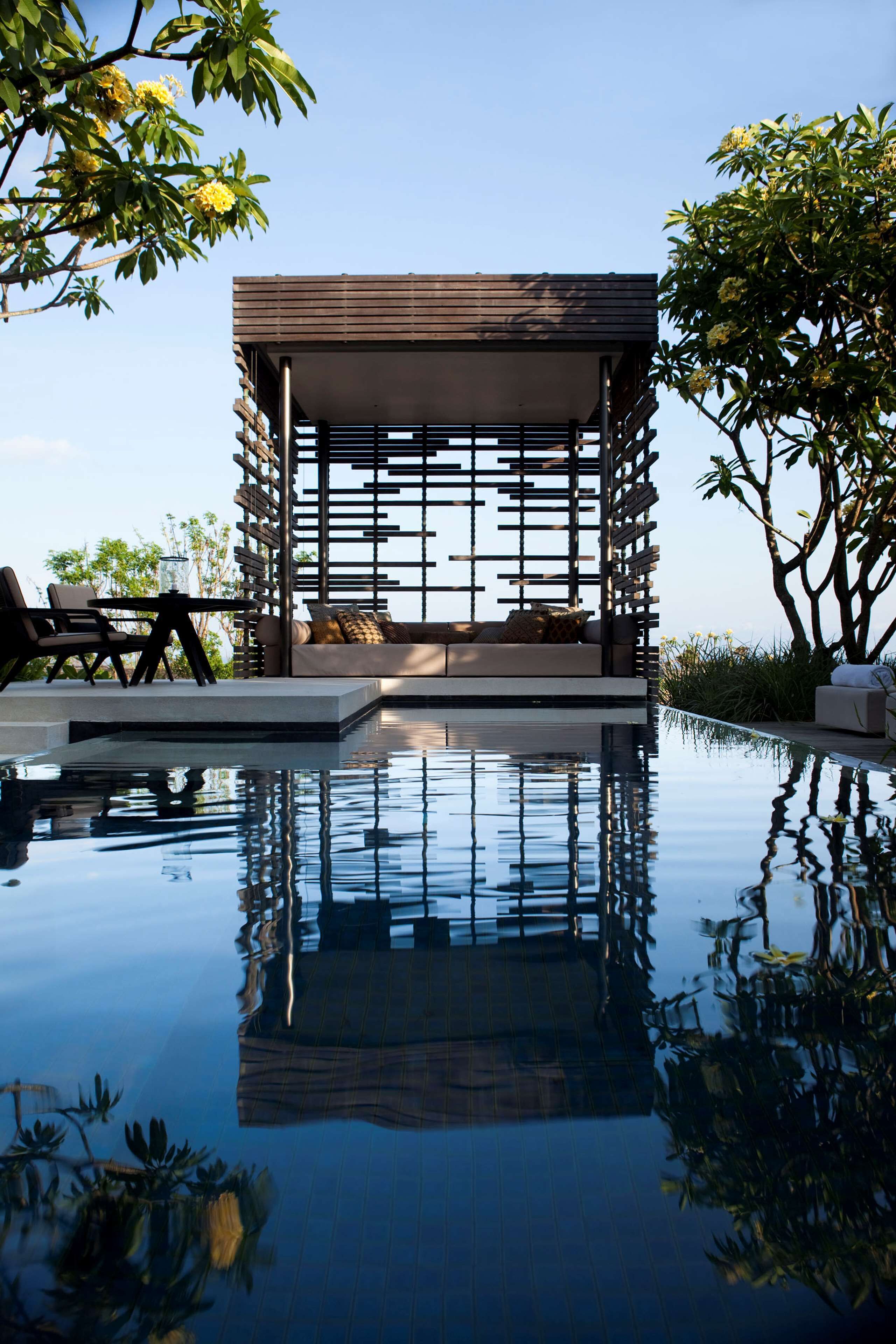A modern outdoor lounge area with a pool, seating, and a wooden pergola structure.