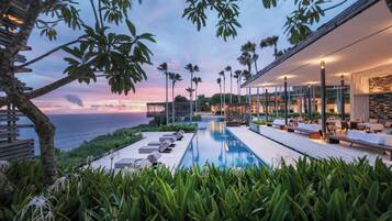 A modern pool area with lounge chairs and a view of the ocean at sunset.
