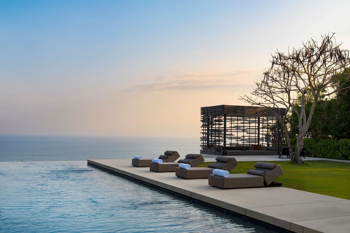A poolside area with lounge chairs and a wooden pergola overlooking the sea.