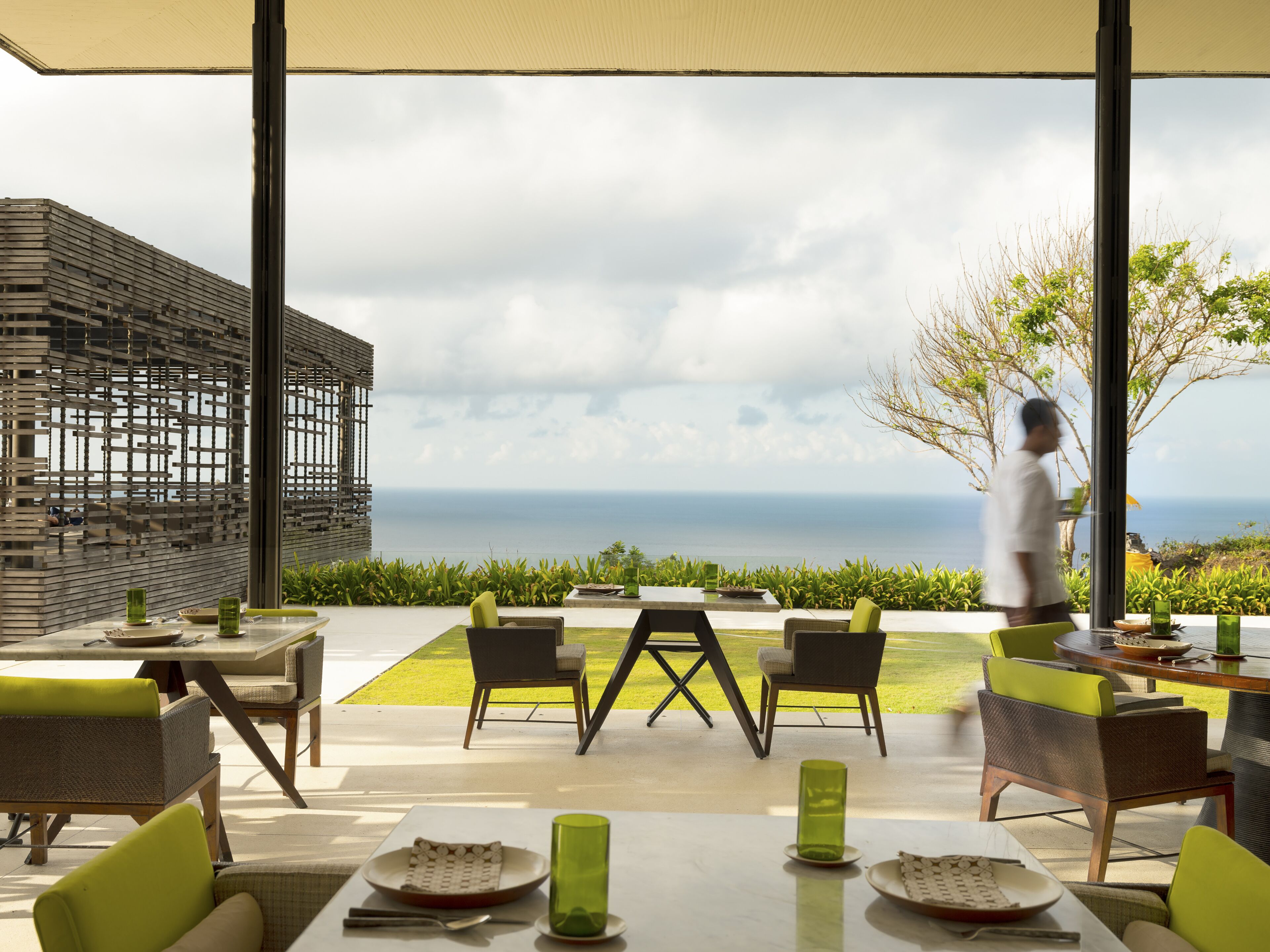 An outdoor dining area with a view of the sea, featuring modern furniture and a large umbrella.