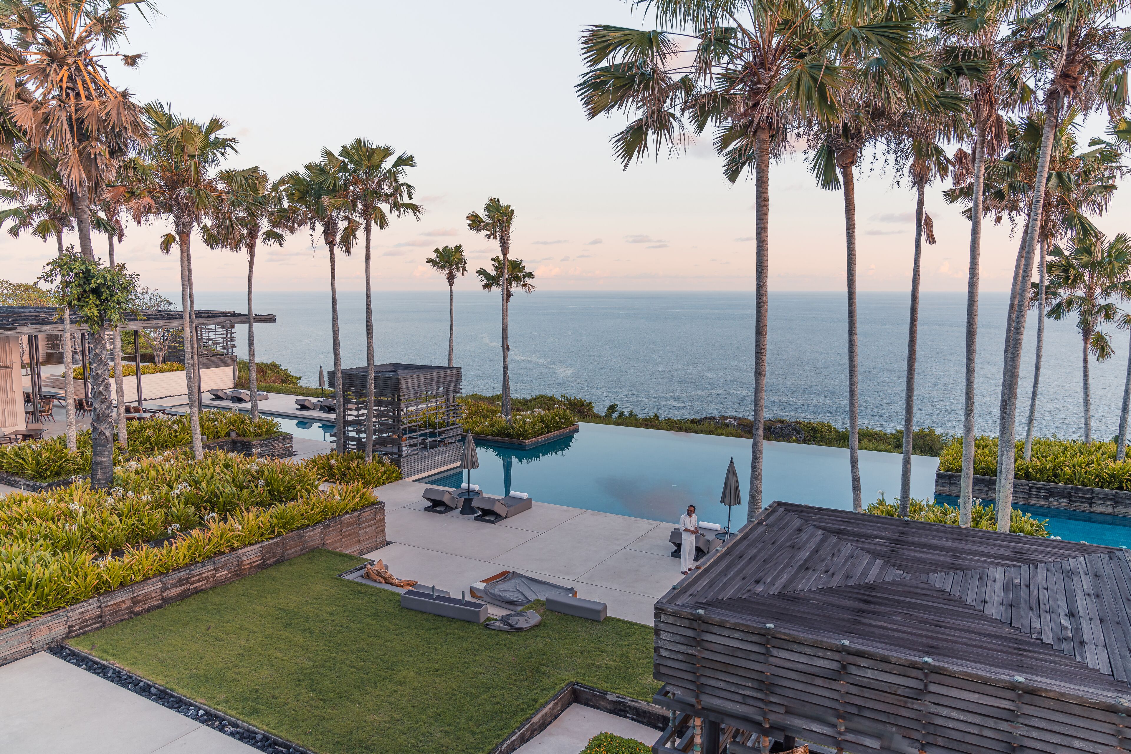 Zona de piscina con sillones, terraza de madera y palmeras con vistas al océano.