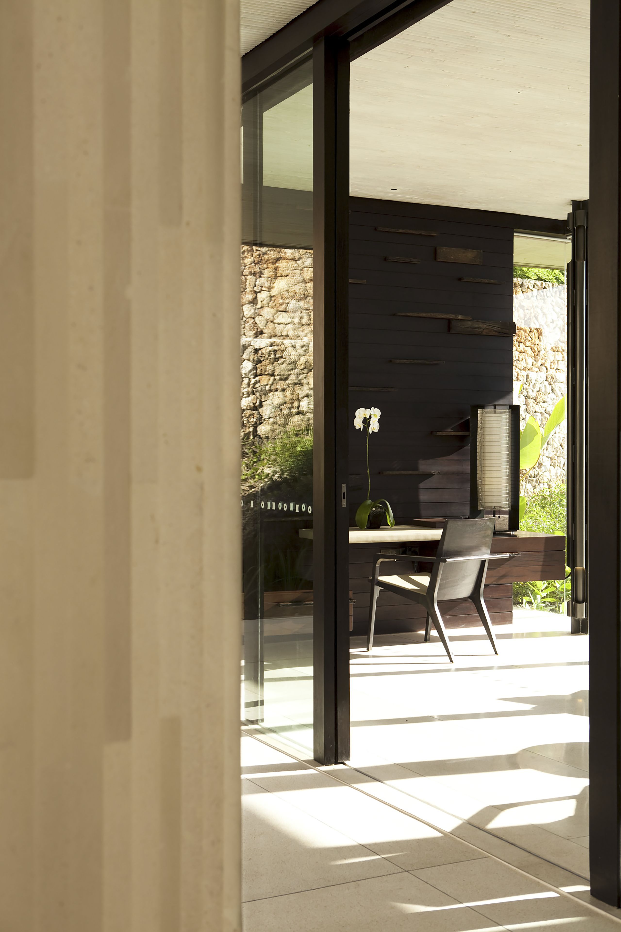 Een modern interieur met een glazen deur naar een buitenruimte, een stenen muur en een minimalistische zithoek.
