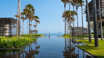 Zona de piscina con palmeras, una persona caminando y vista al océano.