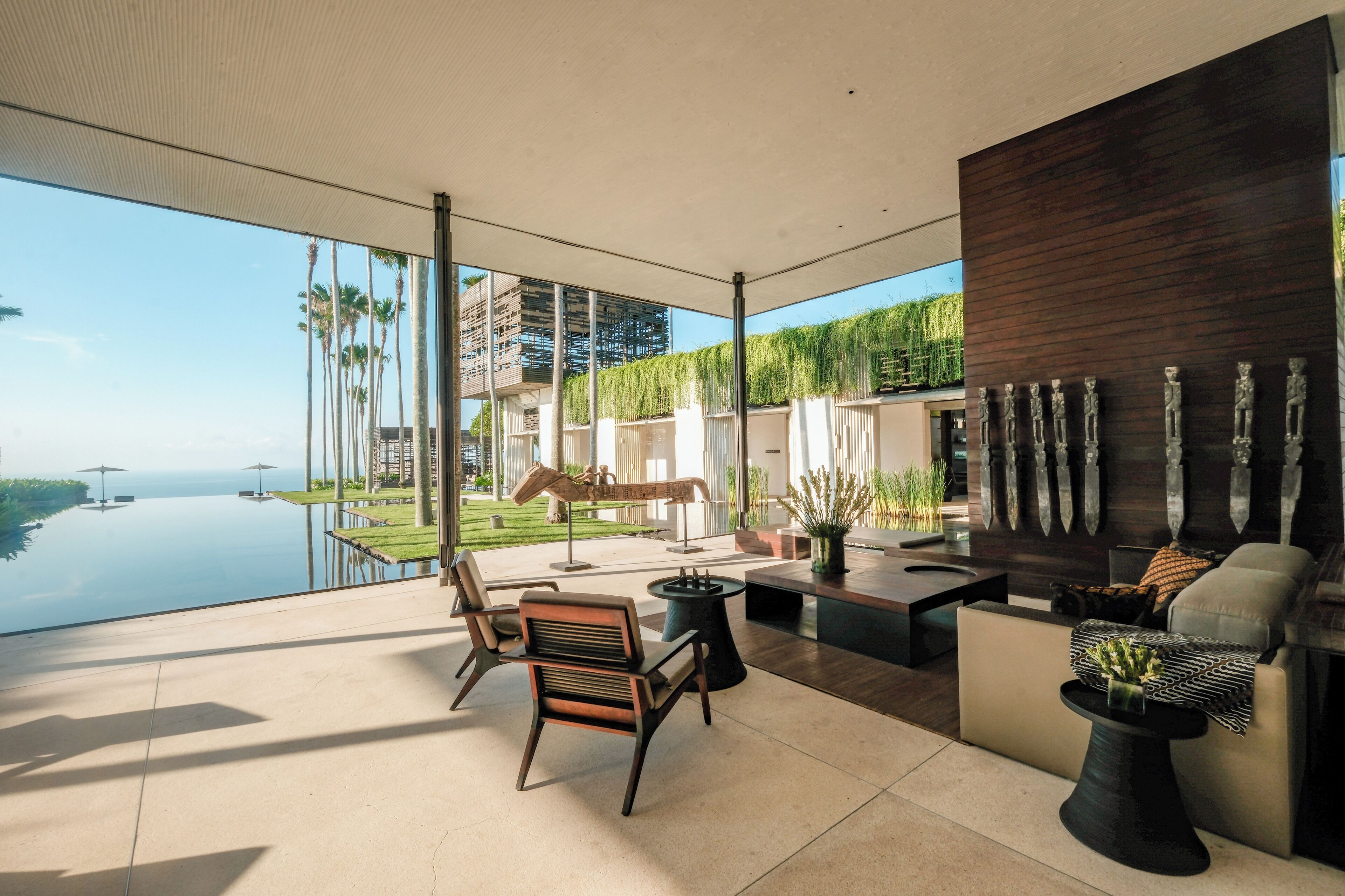 A modern outdoor lounge area with a view of a pool and palm trees, featuring contemporary furniture and a wooden accent wall.