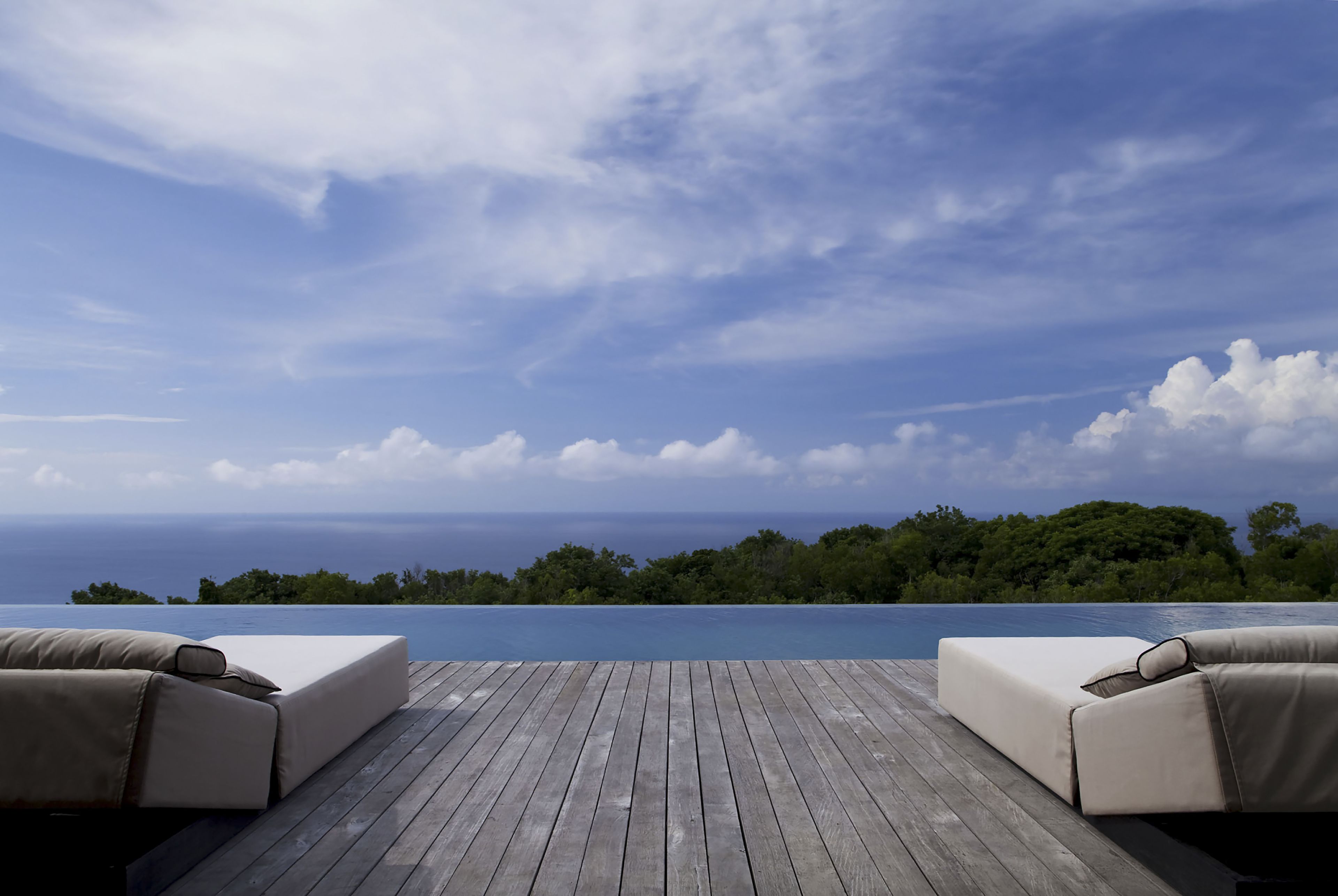A wooden deck with two beige sofas facing a pool and ocean view.