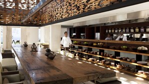 A spacious dining area with a long wooden table, wicker chairs, and shelves with kitchenware.