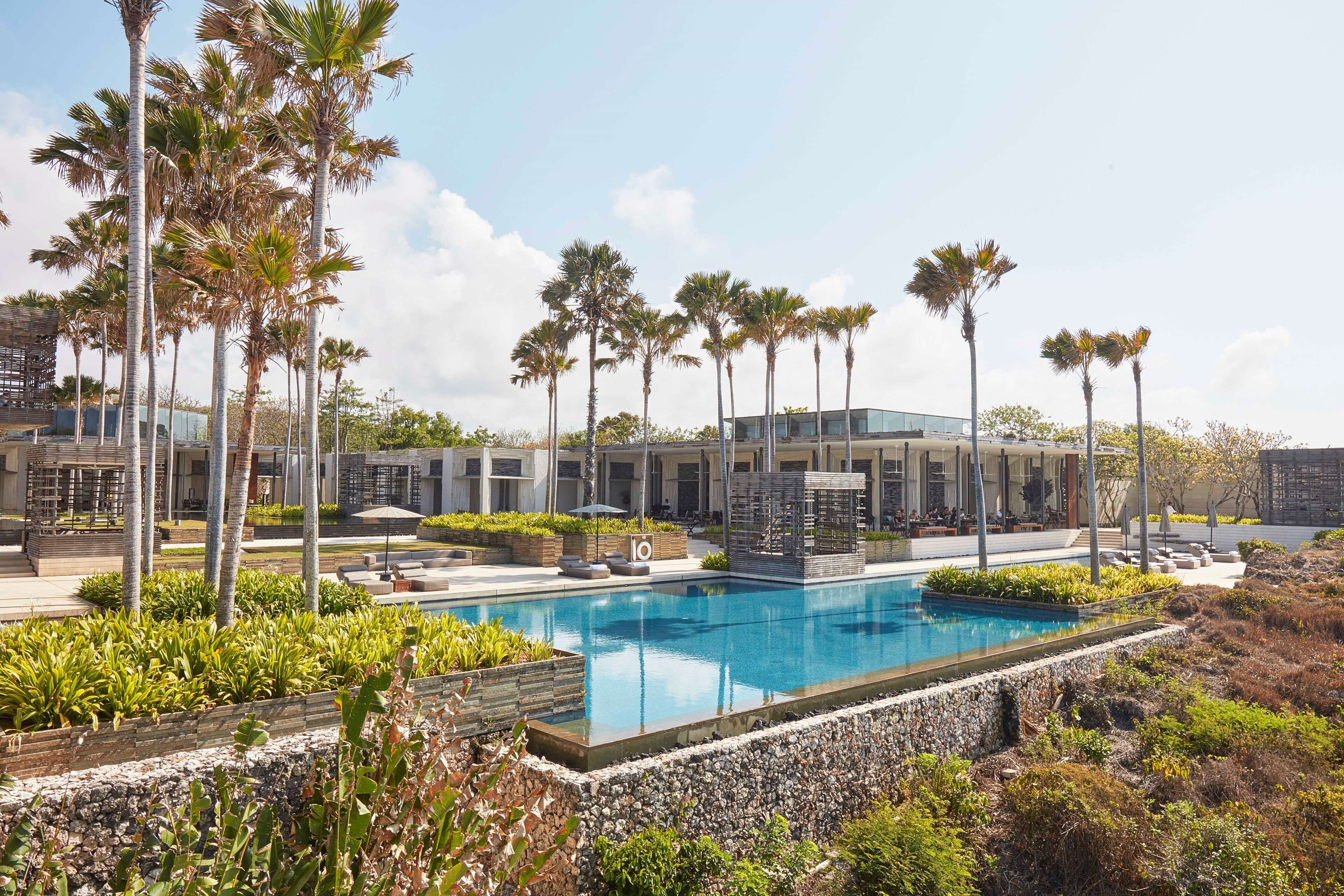 A modern hotel with a swimming pool, palm trees, and a landscaped garden.