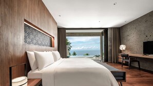 A modern hotel room with a large bed, a desk, and a view of the ocean. - Alila Villas Uluwatu, Bali (Pecatu)