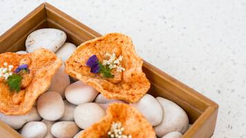 A wooden box containing three triangular food items with white pebbles and small flowers.