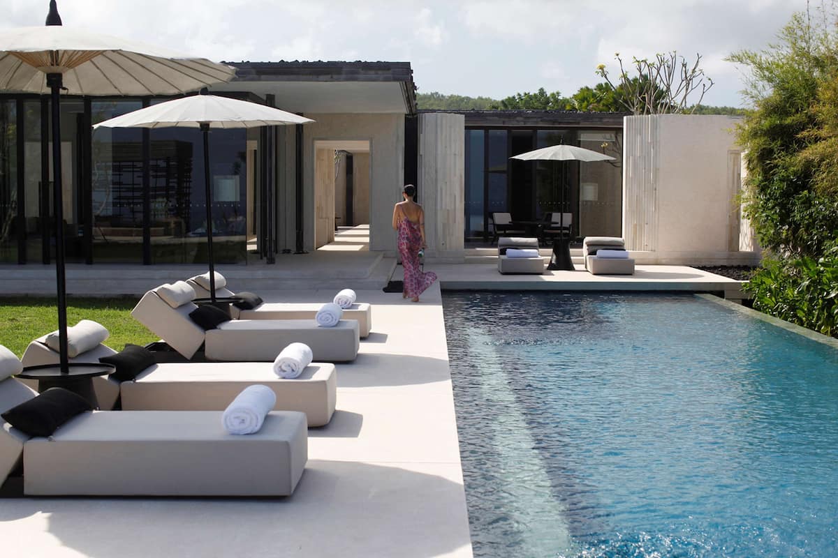 A modern outdoor pool area with lounge chairs and umbrellas, a clear blue pool, and a pathway leading to a building.