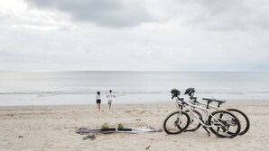 A beach with a bicycle and a blanket on the sand.