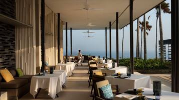 A restaurant with tables set for dining, overlooking a scenic ocean view.