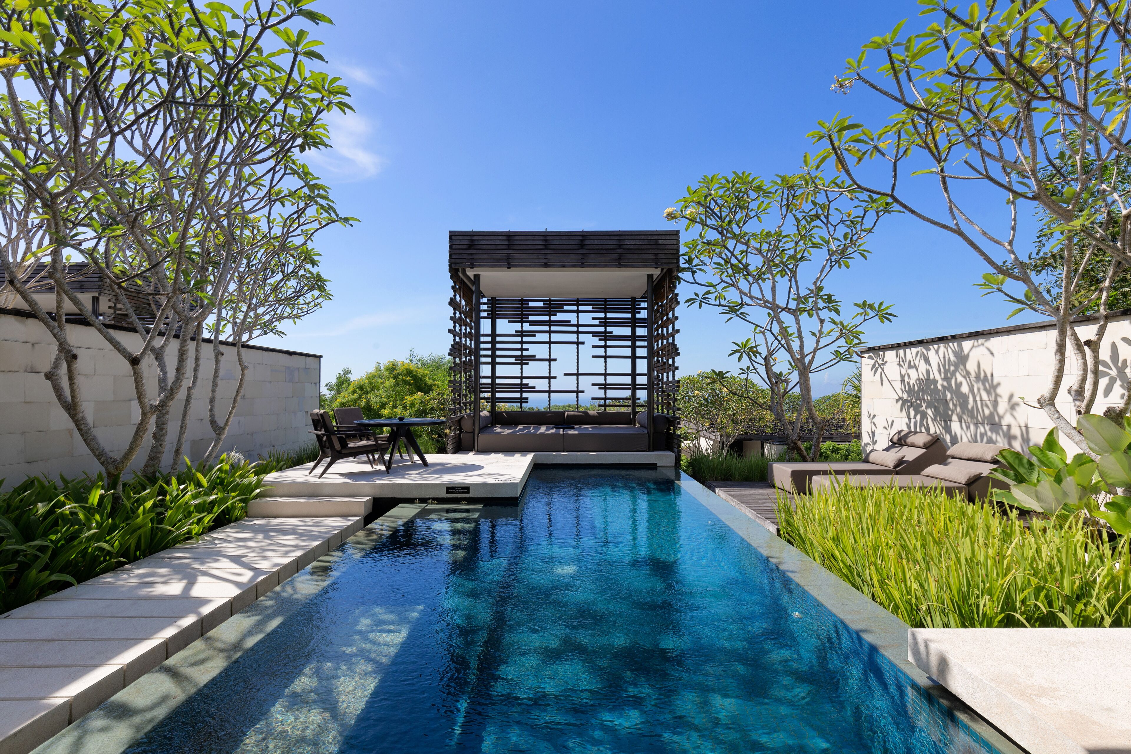 A modern outdoor pool area with a geometric water feature, seating, and lush greenery.