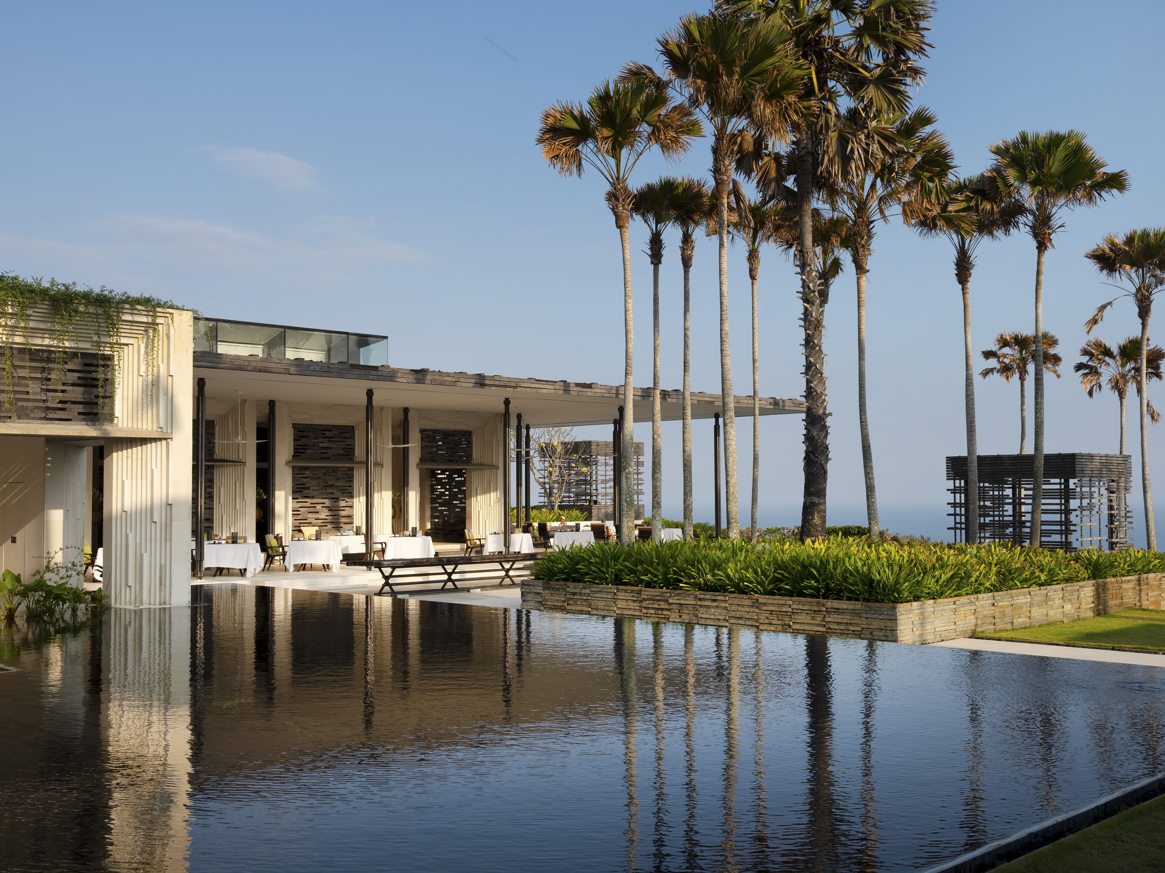 A modern building with a pool, palm trees, and a view of the ocean.